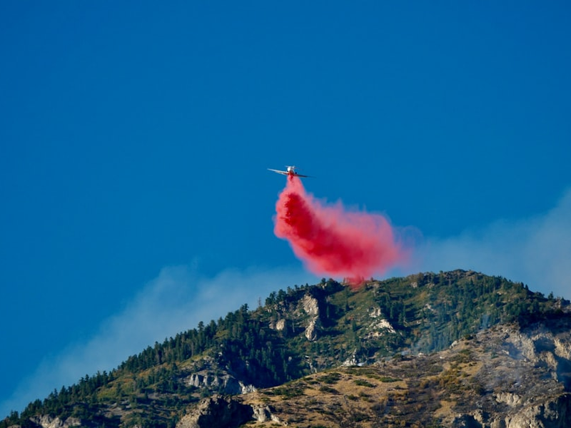 Firefighting plane drops red retardant on mountain.