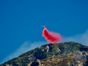 Firefighting plane drops red retardant on mountain.