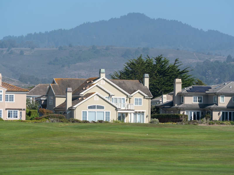 Suburban houses on a green lawn with hills behind.
