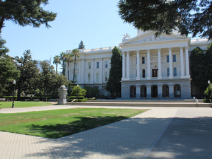 Neoclassical Capitol Building with Lawn and Palm Trees A stately neoclassical building viewed from a distance, featuring a manicured lawn and palm trees in the foreground. Sunny, calm weather evokes institutional grandeur.