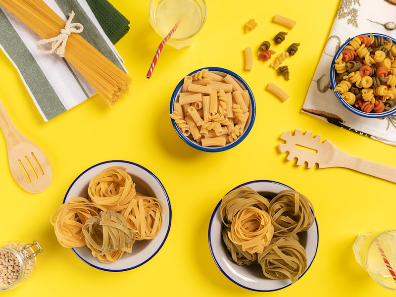 three bowls of pasta sit on a yellow surface