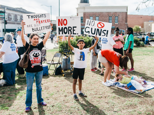 A North Texas mother and her son hold protest signs at the March for Our Lives sister rally in Denton, Texas on March 24th, 2018. In the background, volunteers register people to vote.