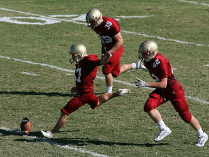 College player prepares to kick the ball to start the game.  His teammates prepare to accompany him downfield.