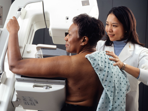 Woman Receives Mammogram.  An Asian female technician positions an African-American woman at an imaging machine to receive a mammogram.  Creator: Rhoda Baer