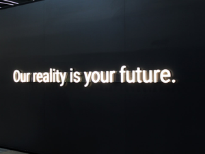 a black wall with a neon sign that says our reality is your future