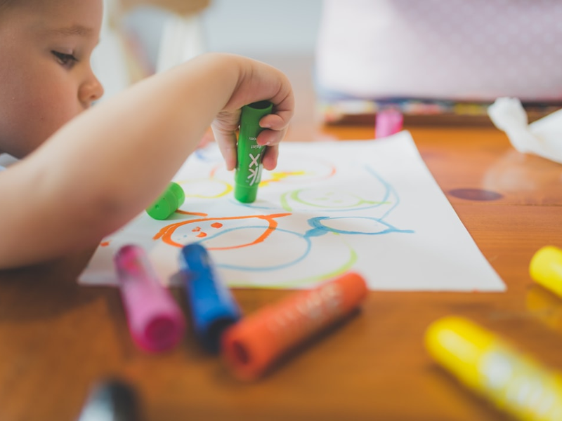 a little boy that is sitting at a table with some crayons