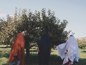 Three people in ghost costumes stand near a tree.