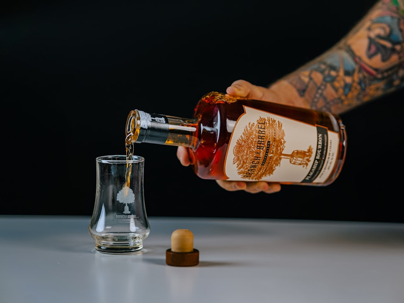 Tattoo arm pouring a neat pour of bourbon into a glass.