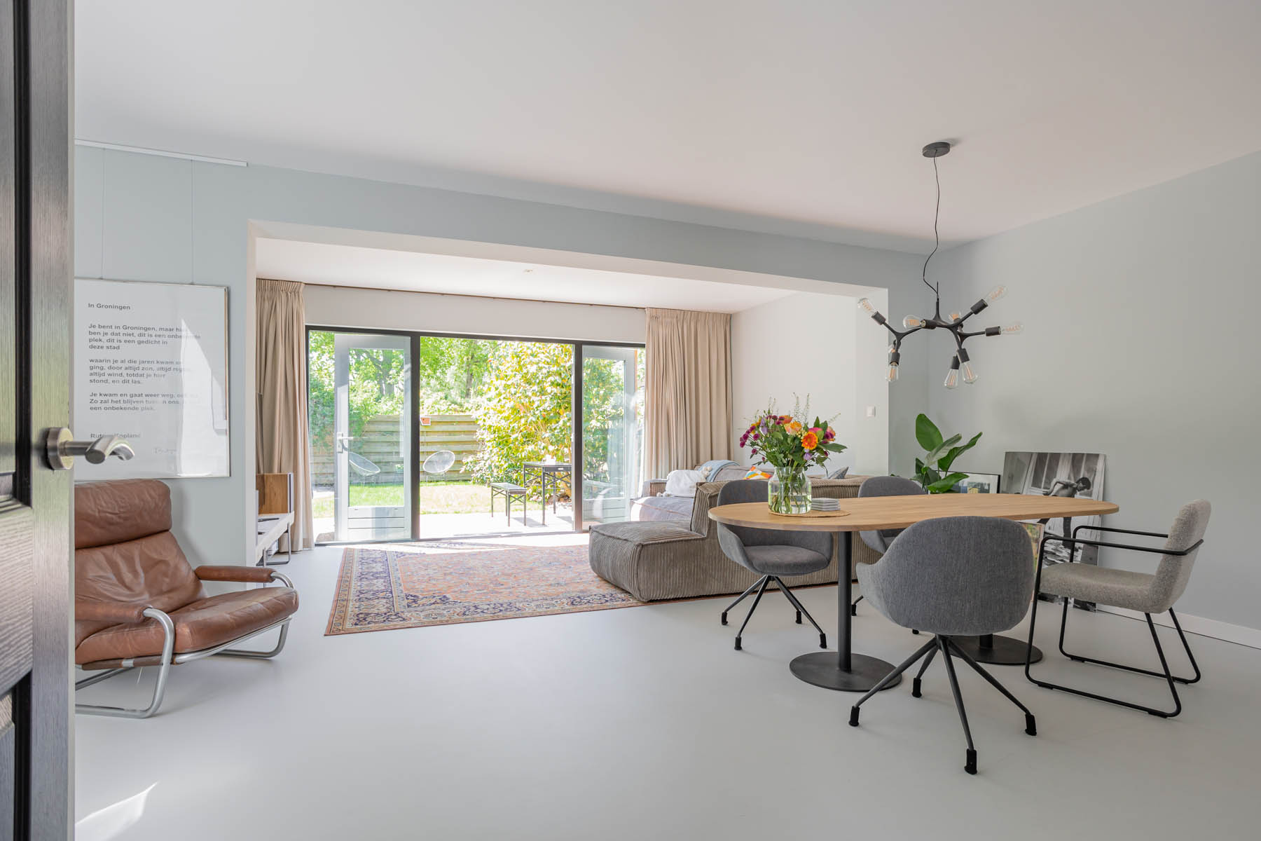 Open woon-eetkamer met leren fauteuil en tuin-uitkijk, professionele vastgoedfotografie