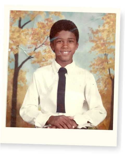 Childhood school portrait of Alex Jones wearing a white shirt and tie against an autumn backdrop
