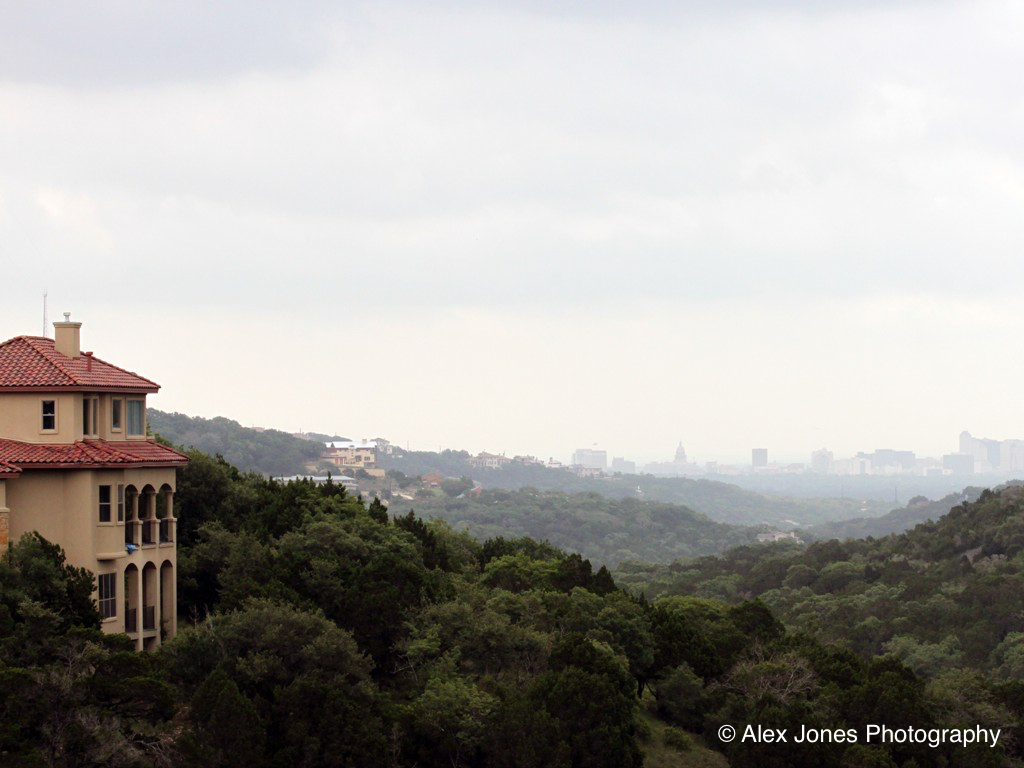 This picture shows a house on a hill with lots of green trees around it. In the distance, you can see a city with tall buildings.