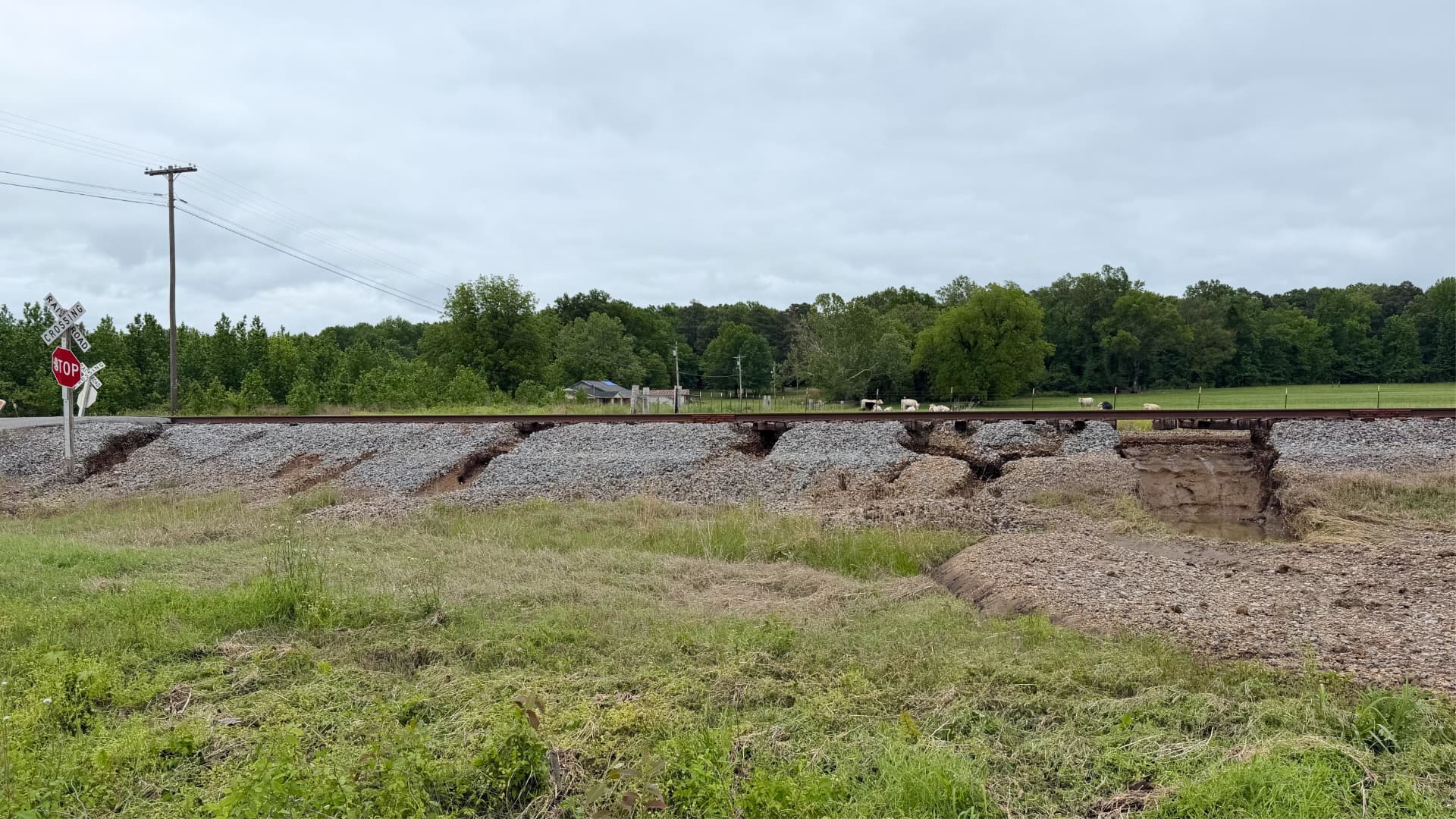This photo shows a railroad track that has been damaged by water. The ground beneath the tracks has washed away, causing parts of the track to sag and break apart.
