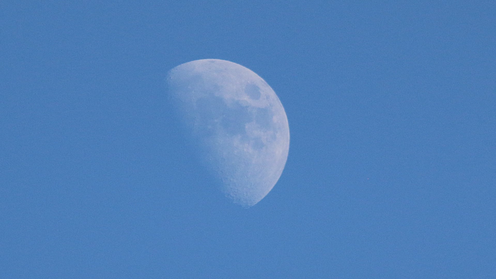 This image shows the Moon in the daytime sky. Only a portion of the Moon is lit up by the Sun, making it look like a crescent or half-circle.