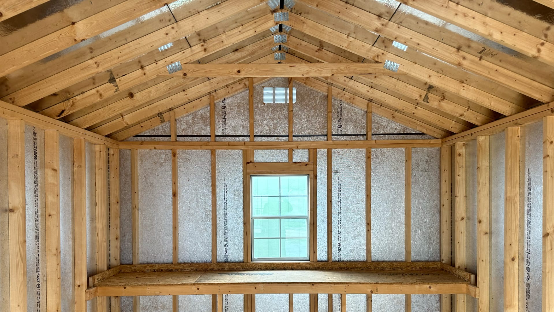 This image shows the inside of a wooden structure under construction, with exposed wooden beams, insulation material, and a window.