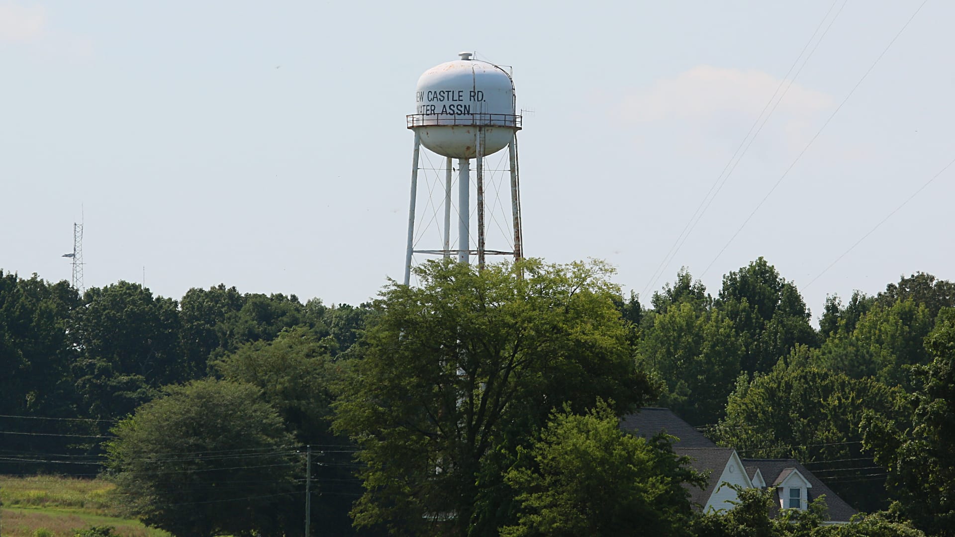 This photo shows a tall water tower standing above a landscape of trees and houses.