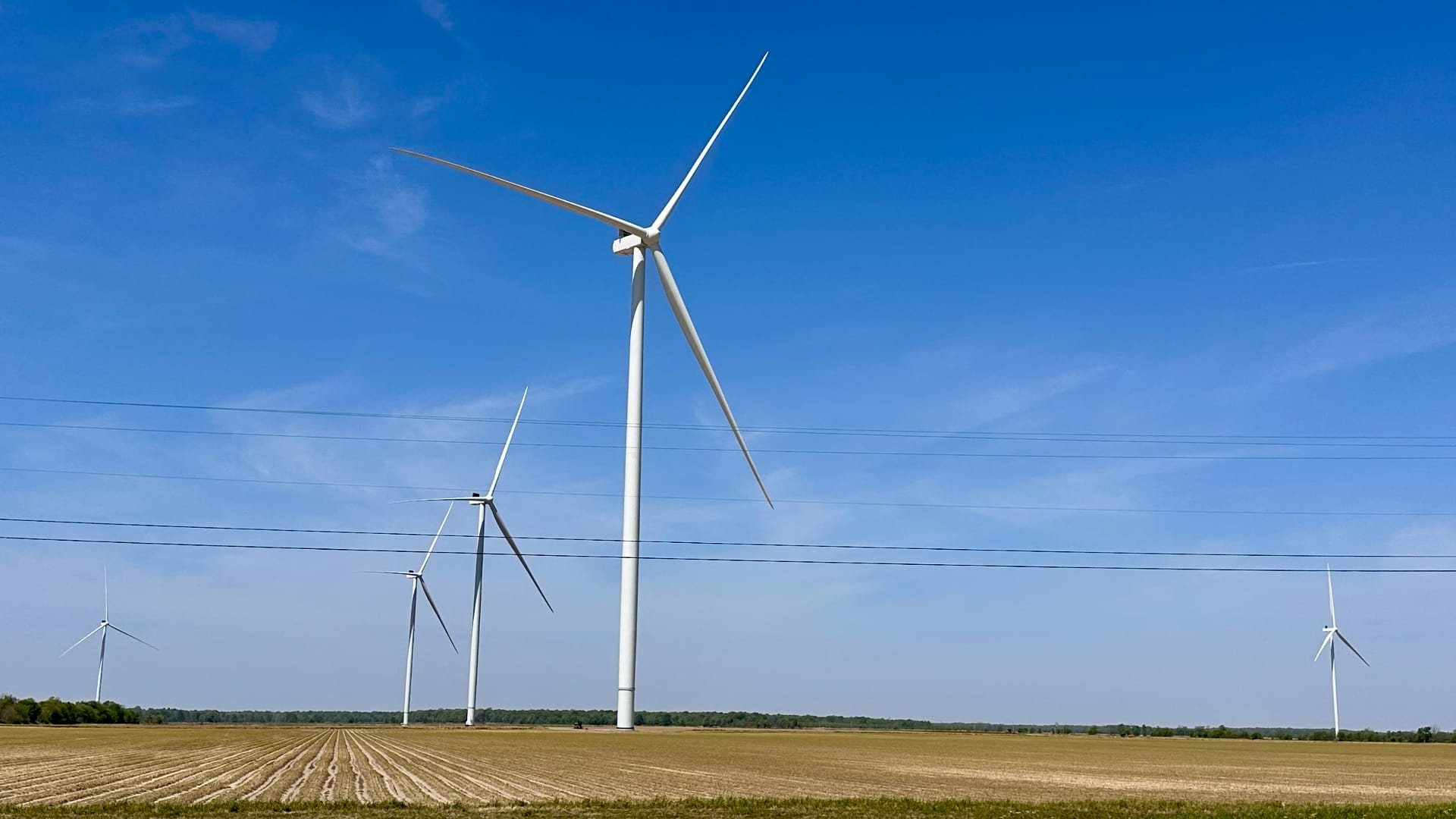 This image shows several large wind turbines in a flat, open field with clear blue sky.