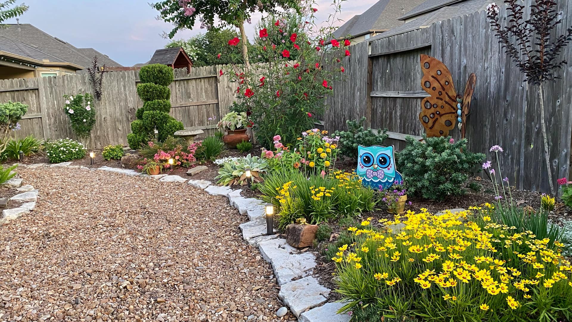 This image shows a garden with many different types of plants and flowers. There are colorful blooms, green bushes, and a gravel pathway.
