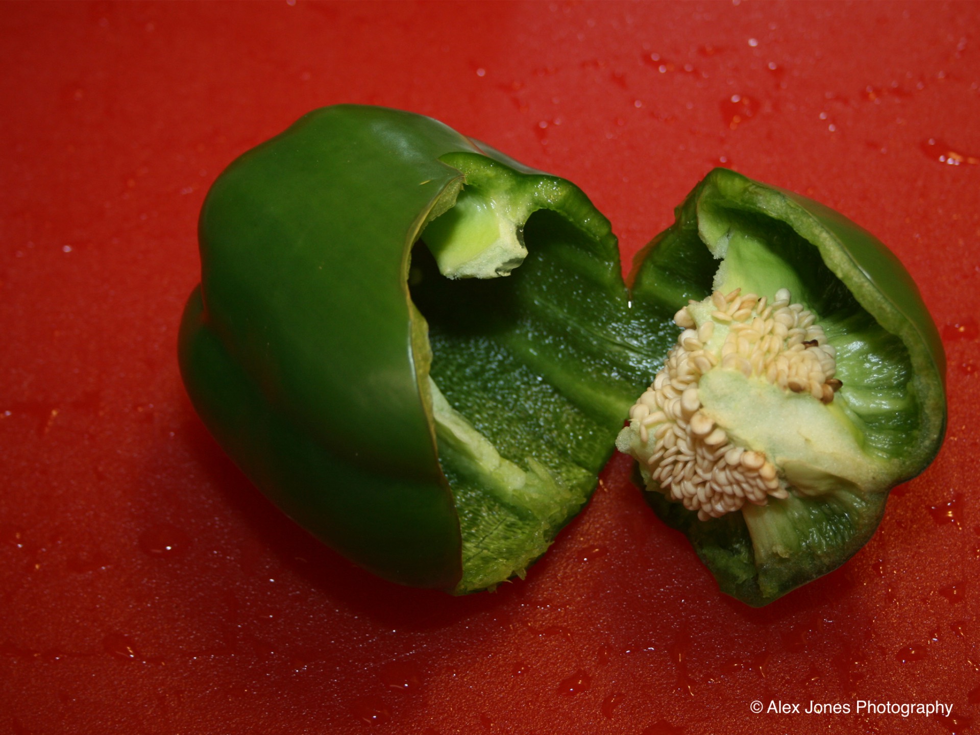 This photo shows a green bell pepper that has been cut in half. You can see the thick green skin on the outside and the white seeds clustered together inside the pepper.