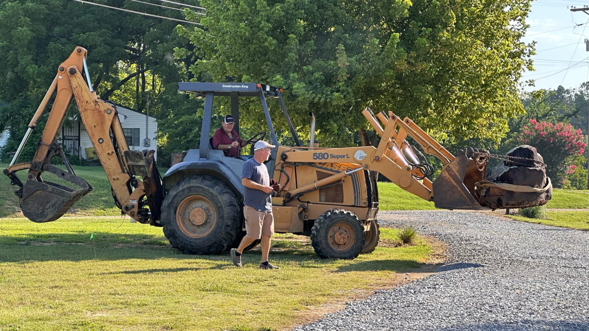 This image shows a large backhoe loader machine at work on a construction site. The machine has a long arm with a bucket on one end that can scoop up dirt and rocks.
