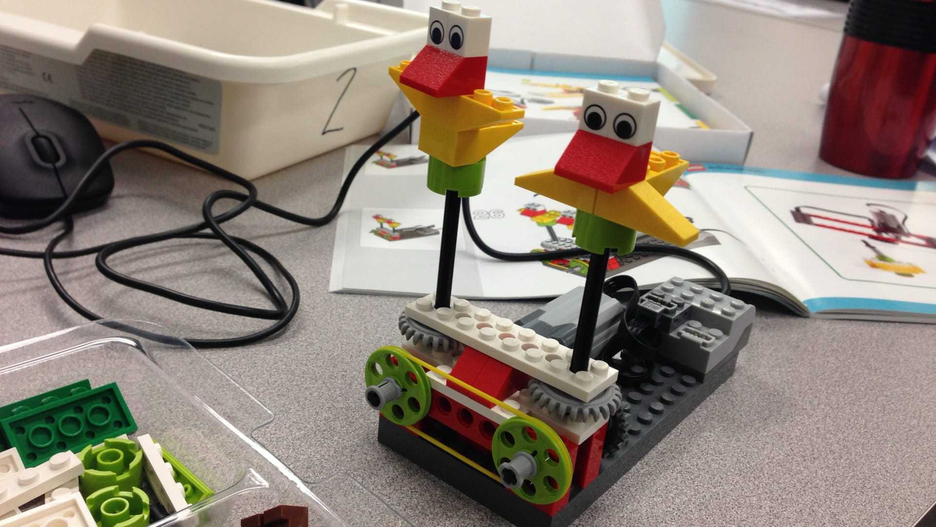 This image shows a LEGO robotics setup with two wheeled vehicles connected to a motor control device via cables.