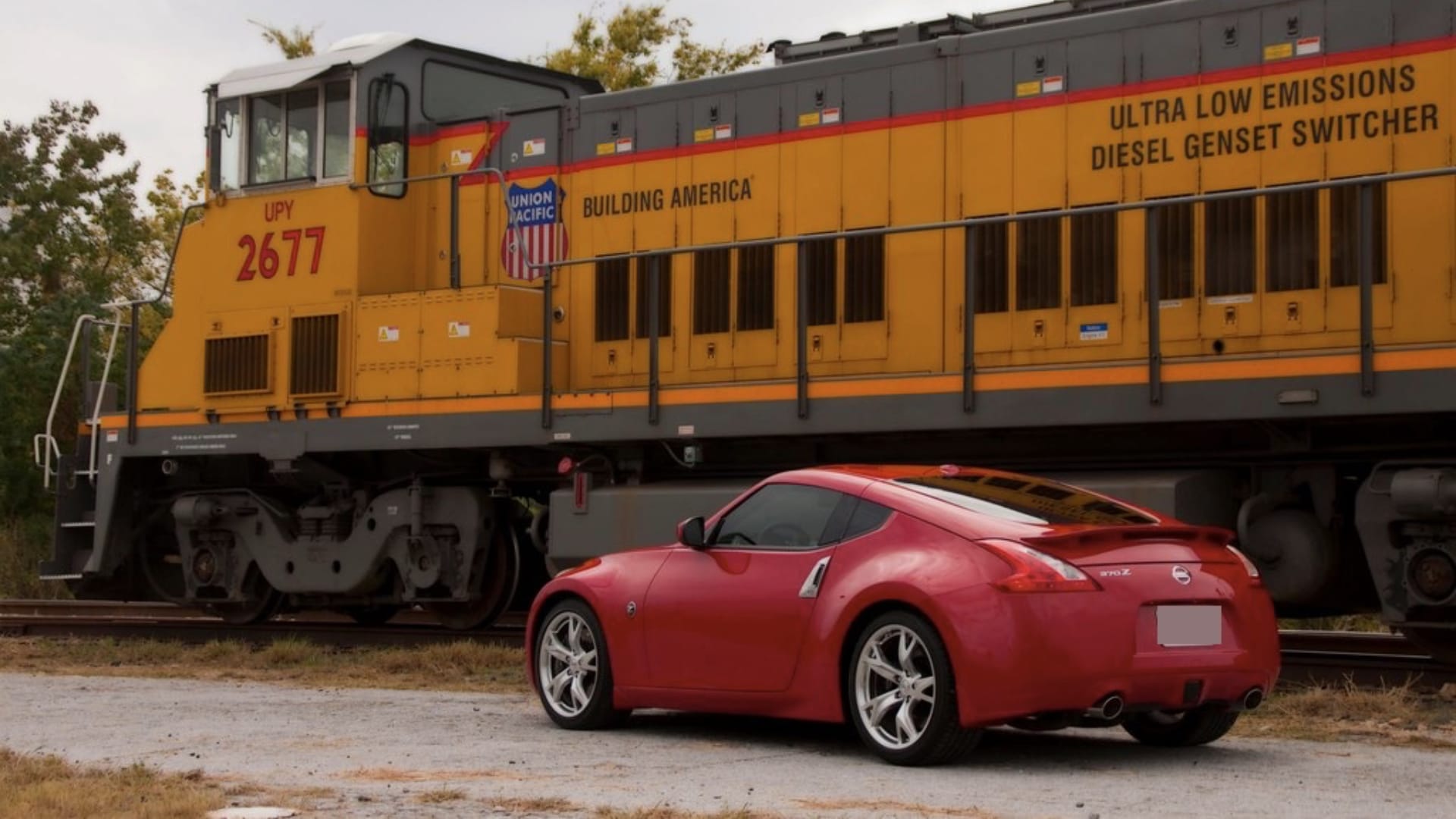 This image shows a large yellow and orange diesel train engine next to a much smaller red sports car on railroad tracks.