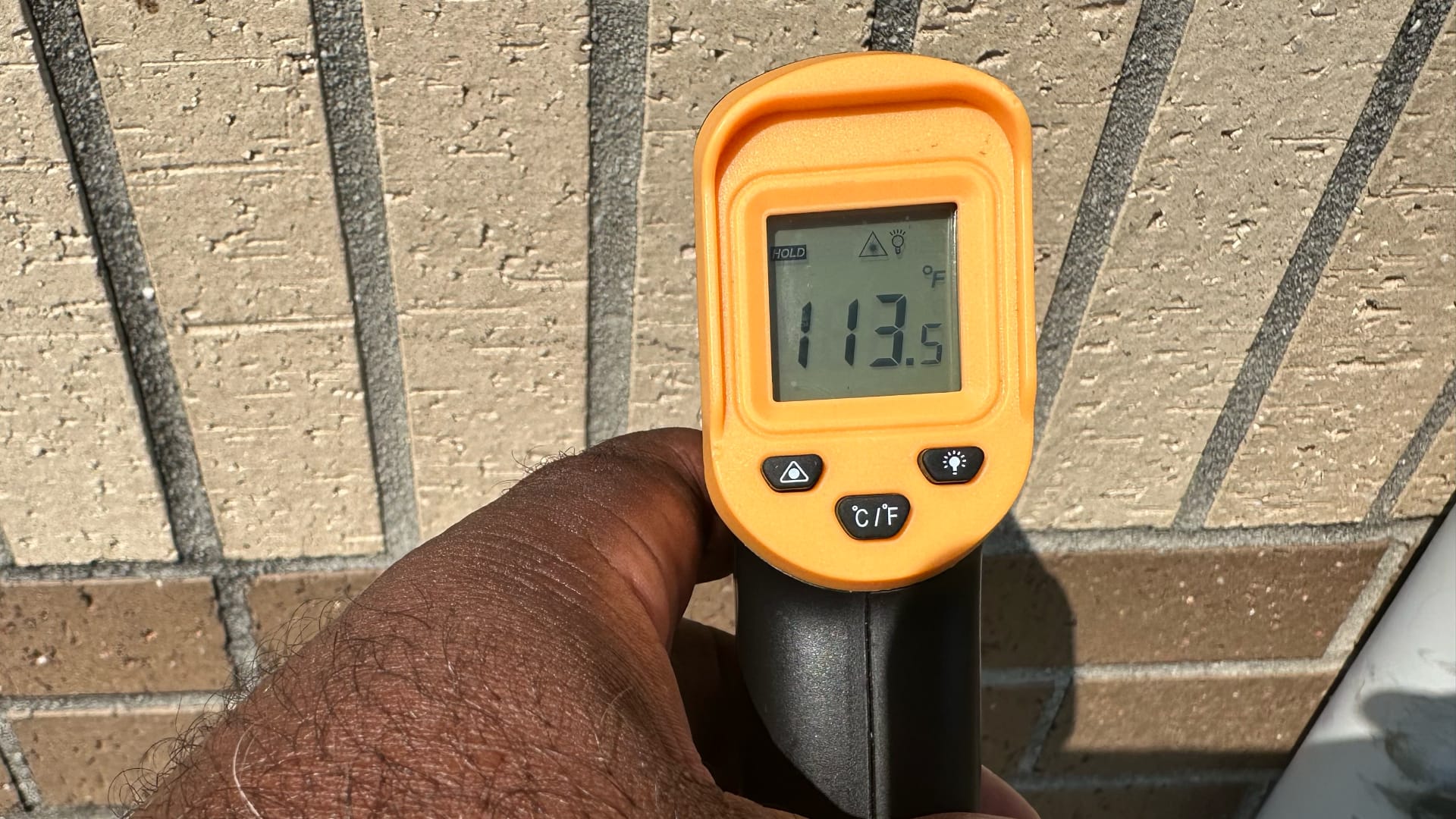 A person is holding an orange infrared thermometer that shows a temperature reading of 113.