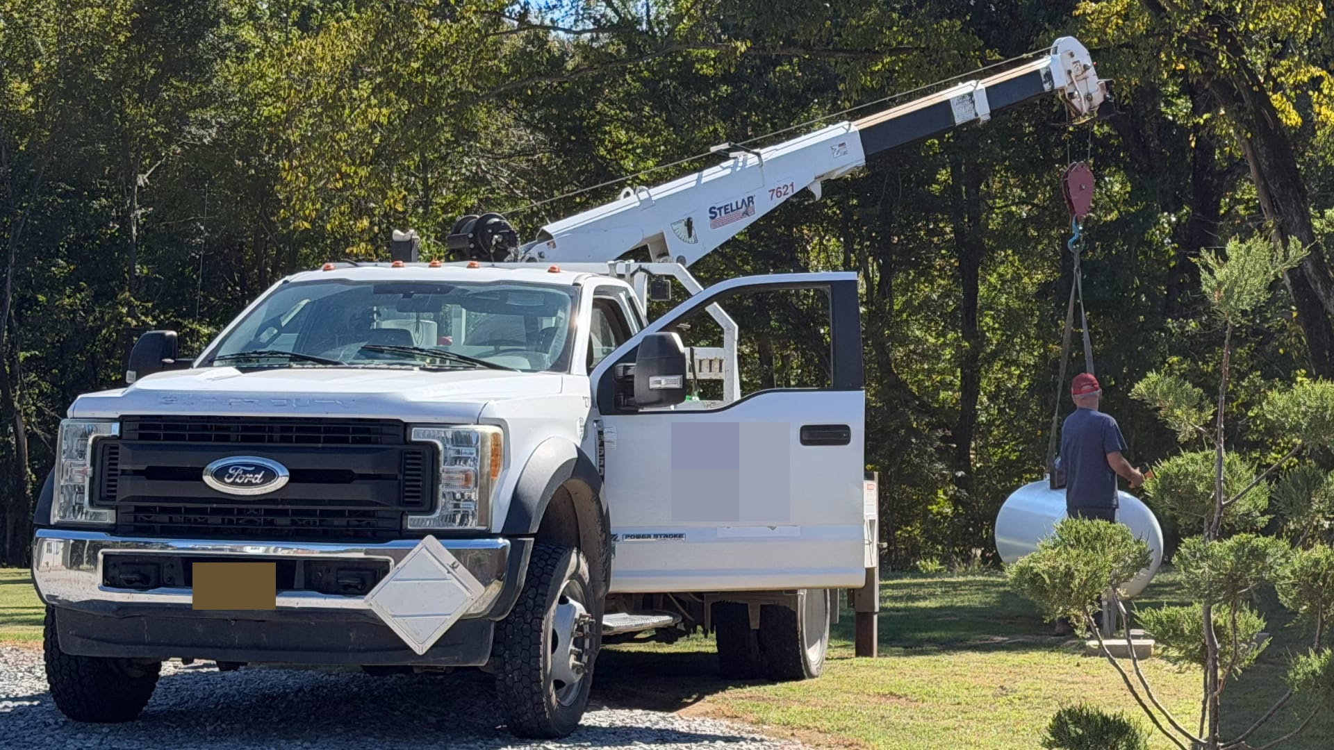 This image shows a white Ford truck with its door open parked next to a tall metal boom lift (marked "Stellar 7621").