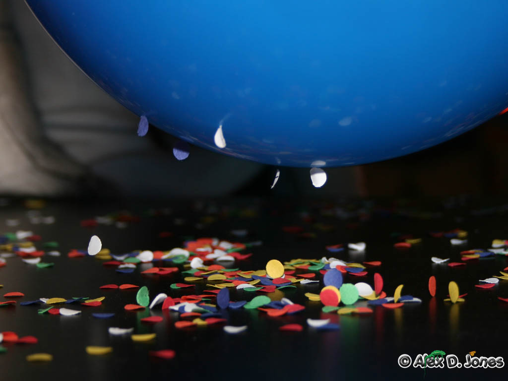A blue balloon floats above a dark surface covered with colorful paper confetti pieces.