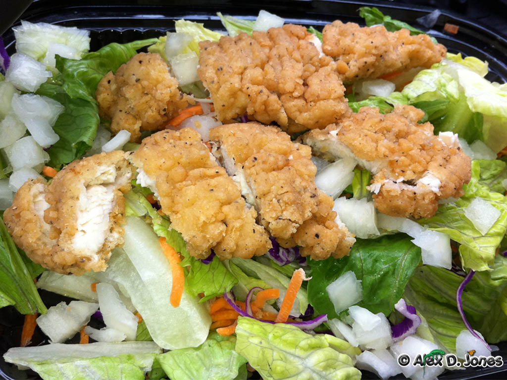 This picture shows golden-brown fried food pieces sitting on top of fresh green lettuce and colorful vegetables.