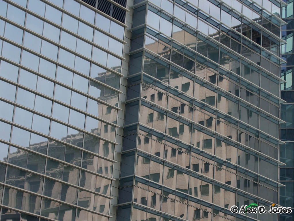 This picture shows a tall glass building that acts like a giant mirror. The glass windows reflect another building, making it look like the second building is inside the first one.