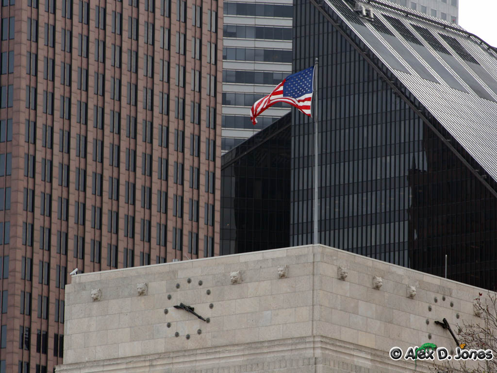 The image shows a tall building with a big clock on it and an American flag waving in the wind.