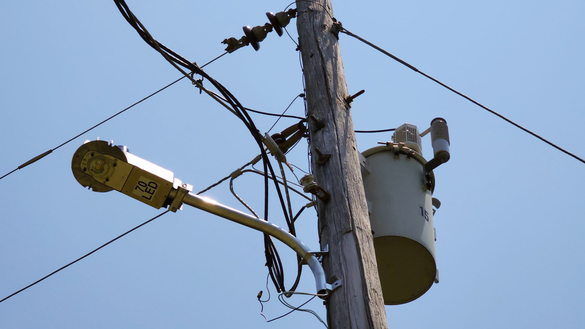 This photo shows a wooden utility pole with a large gray transformer and several wires attached to it.