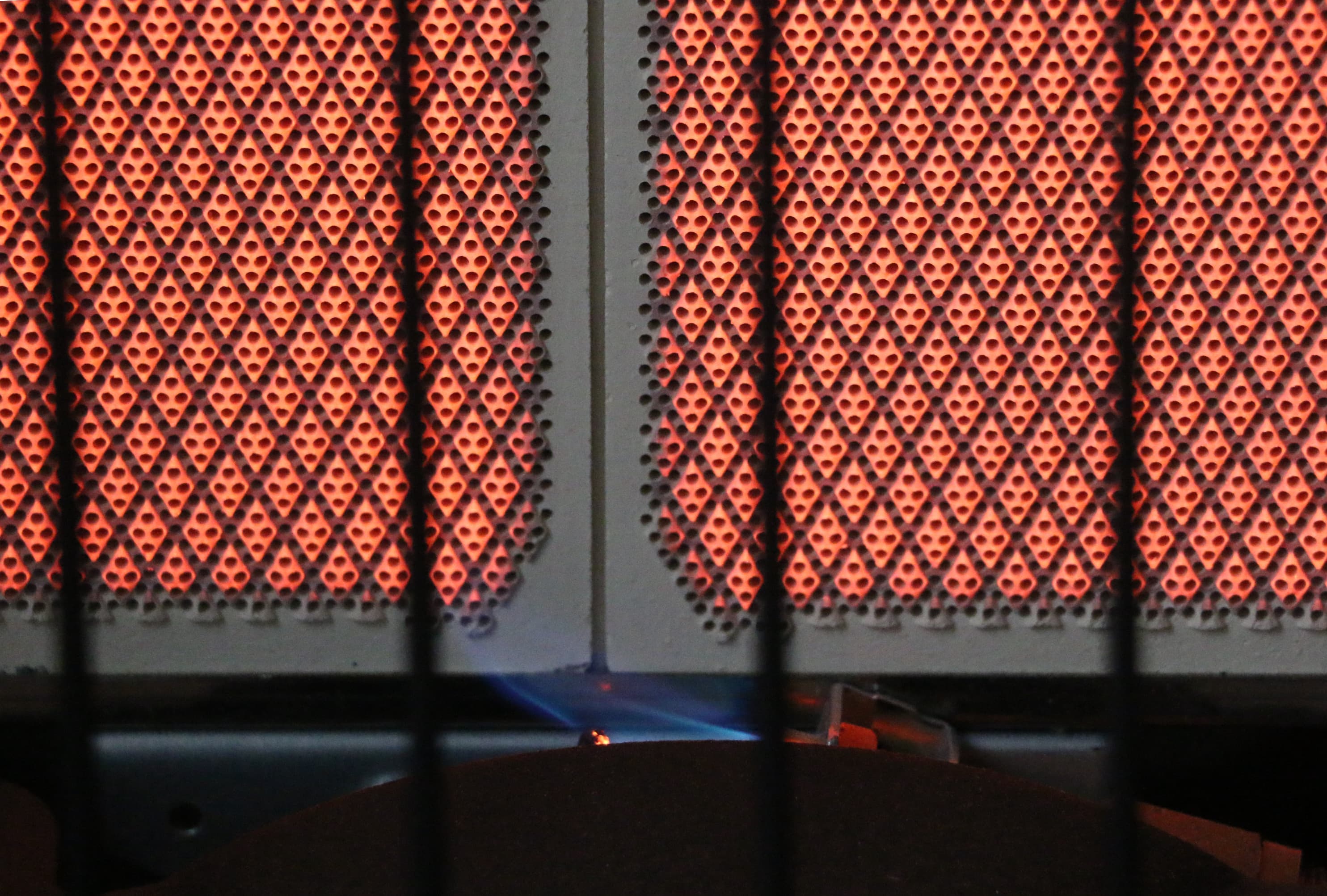 This image shows a propane heater with glowing red heating elements covered by a metal mesh screen.