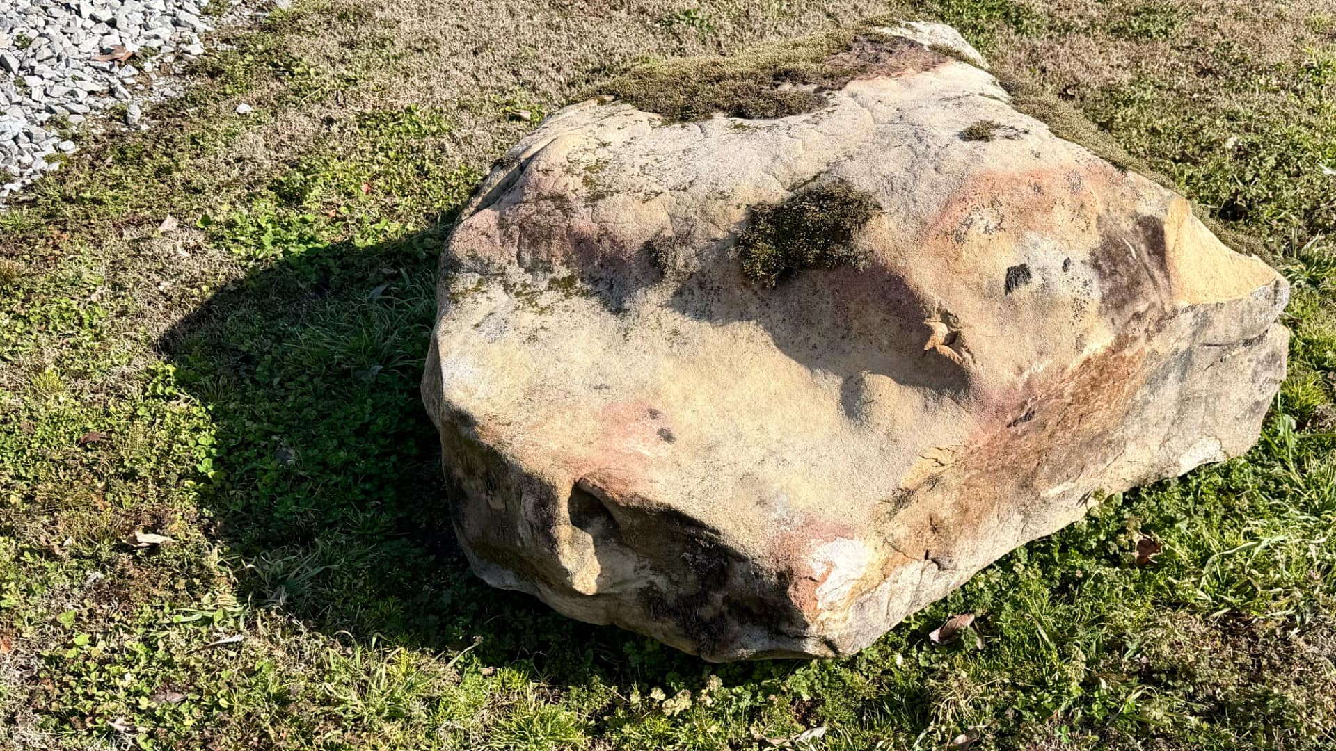 A large rock sitting on the ground has a dark shadow cast on the ground next to it.