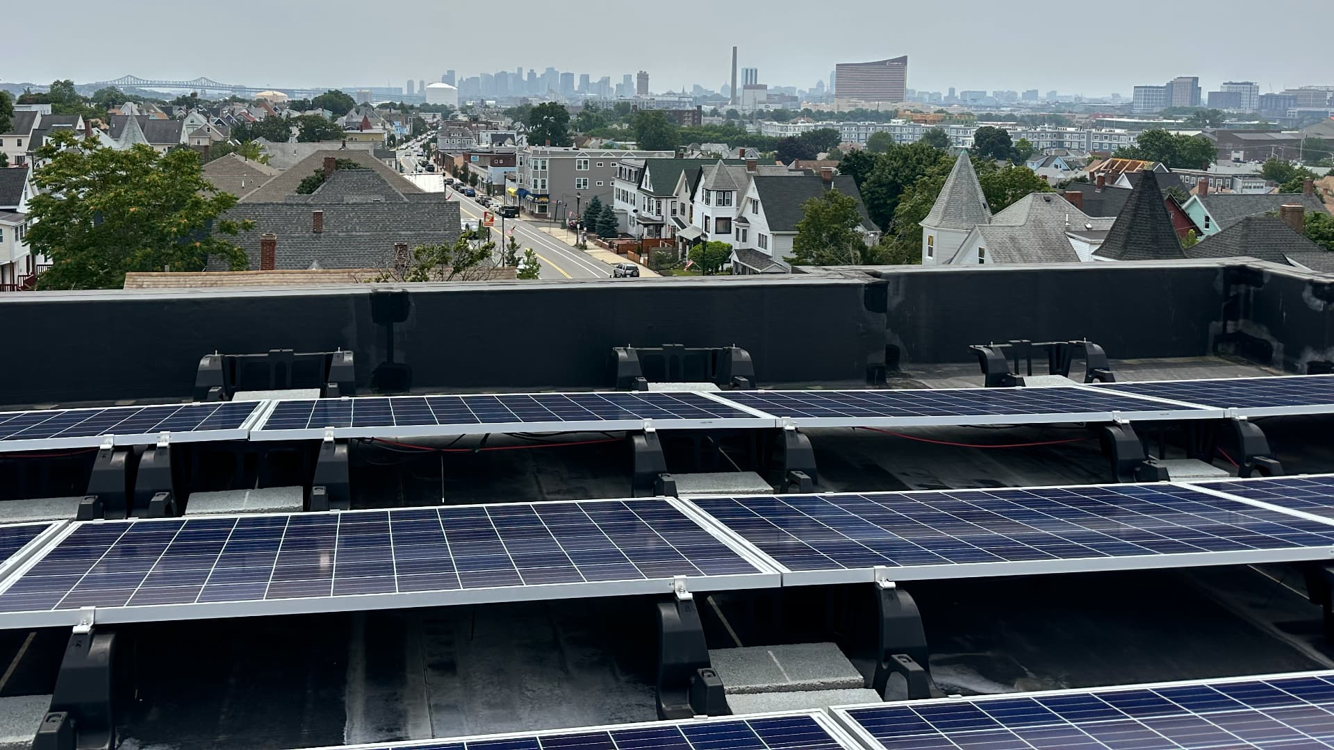 This image shows solar panels installed on a rooftop with a sunny day and a neighborhood visible below.
