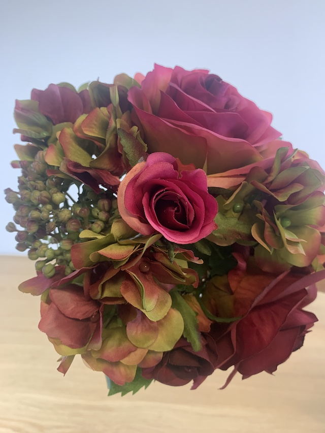 Close-up van een luxe kunstboeket met fuchsia rozen, hortensia's en bessen tegen een lichte achtergrond.