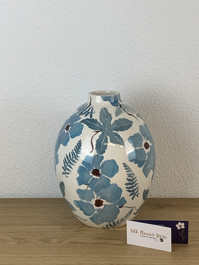 Een ronde witte keramische vaas met een blauw bloemmotief, staand op een houten ondergrond.