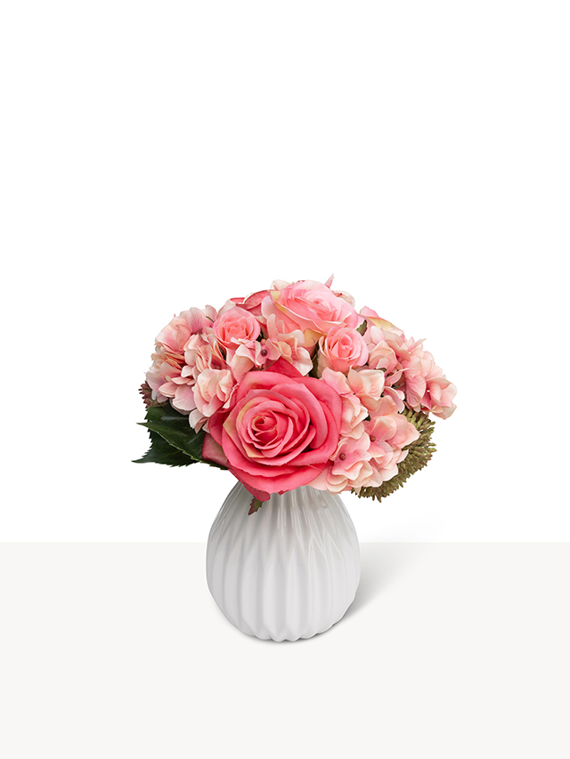 Een verfijnd boeket met bordeauxrode en zachtroze zijden bloemen in een kleine witte geribbelde vaas.