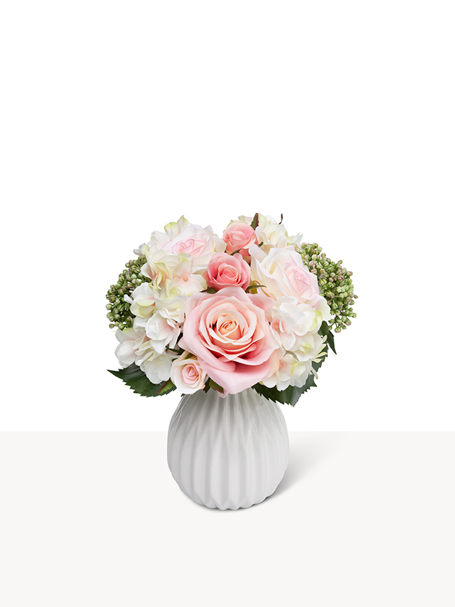Een elegant mini boeket van kunstmatige roze rozen en witte hortensia's in een geribbelde witte keramieken vaas.