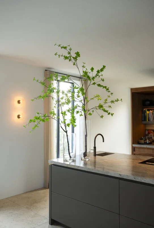 Twee glazen vazen met 150 cm hoge Enkianthus-takken op een modern keukeneiland in een stijlvol interieur.
