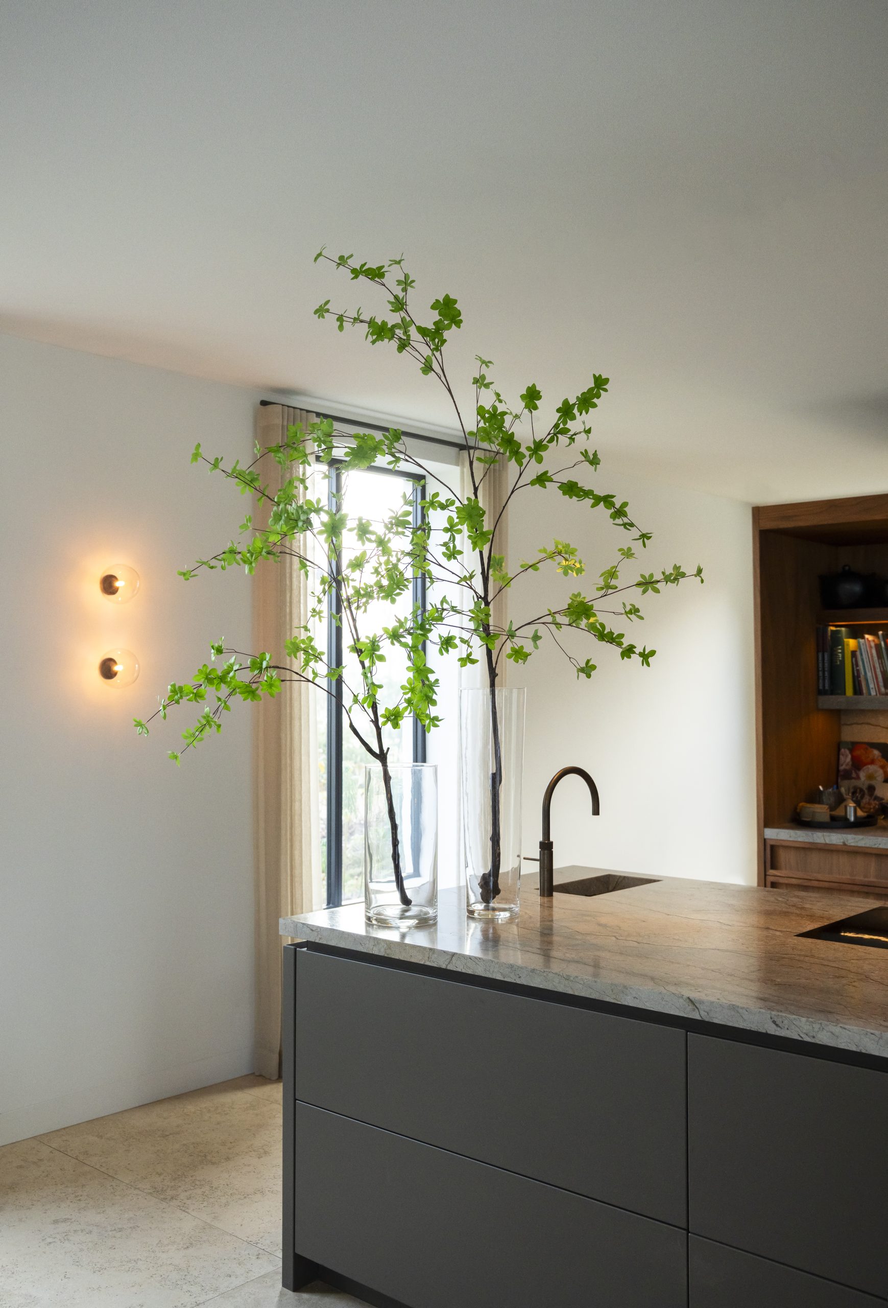 Twee glazen vazen met 150 cm hoge Enkianthus-takken op een modern keukeneiland in een stijlvol interieur.