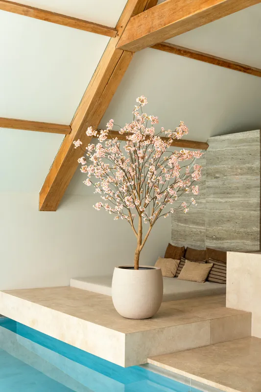 Luxe kunstbloesemboom met zachtroze bloemen in een minimalistische beige pot op een stenen platform.