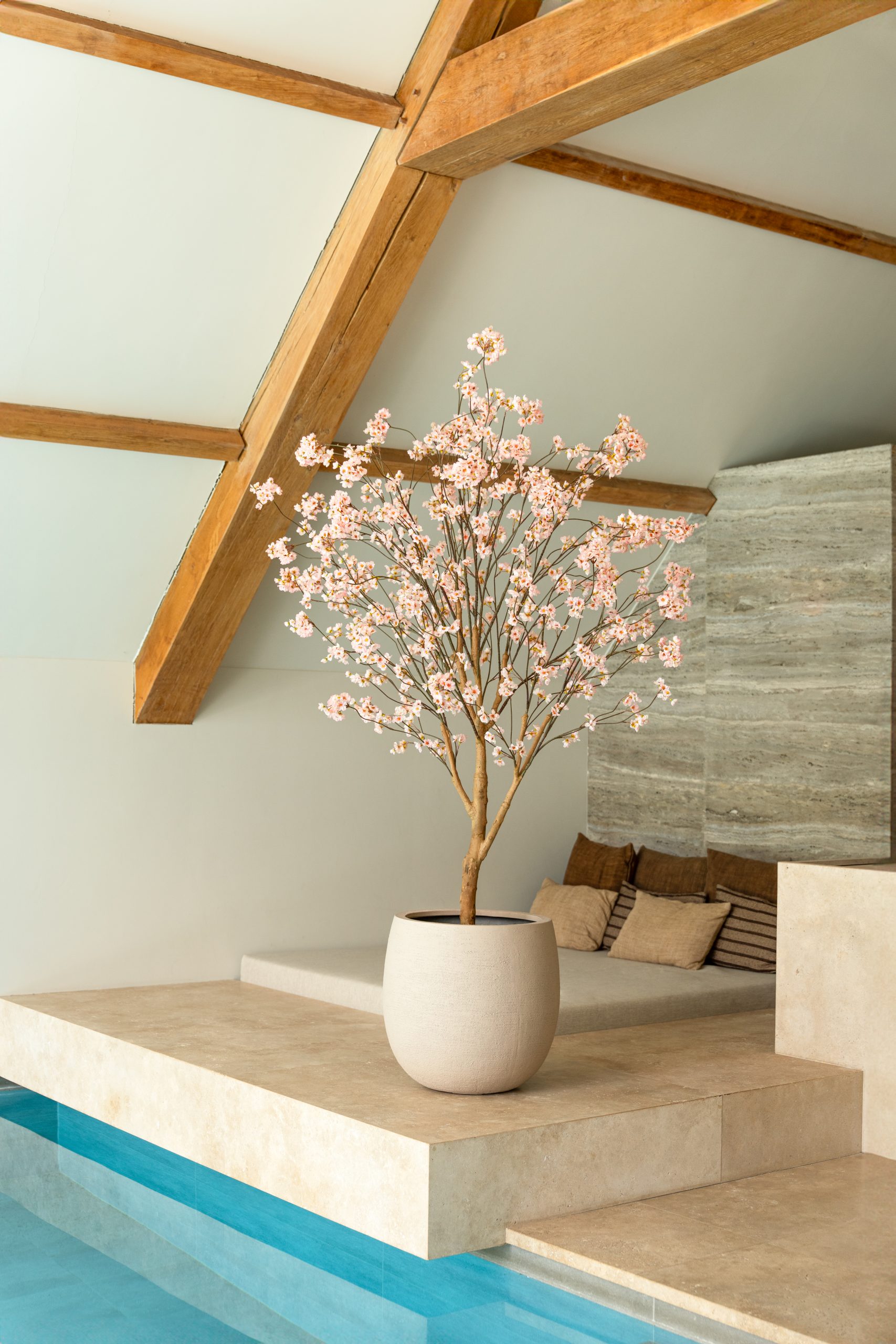 Luxe kunstbloesemboom met zachtroze bloemen in een minimalistische beige pot op een stenen platform.