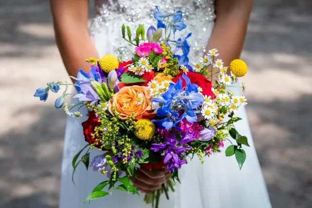 Bruid houdt een kleurrijk boeket van zijden bloemen vast in verschillende tinten zoals oranje, blauw en geel.