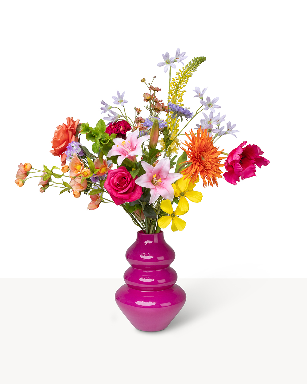 Een weelderig zijden boeket met diverse kleurrijke bloemen in een opvallende glanzende roze vaas.