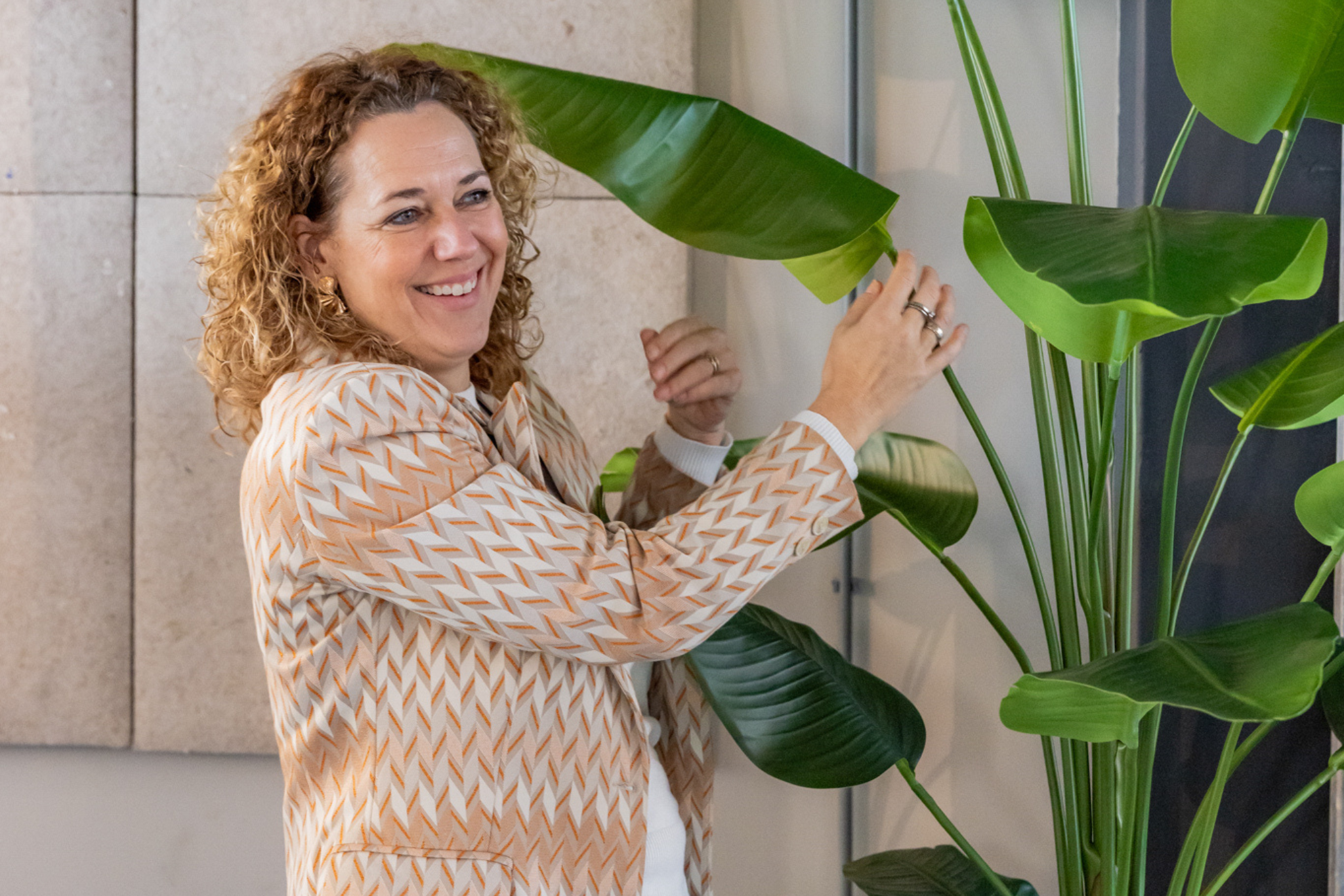 Vrouw met krullend haar controleert de bladeren van een grote kunstmatige kamerplant.