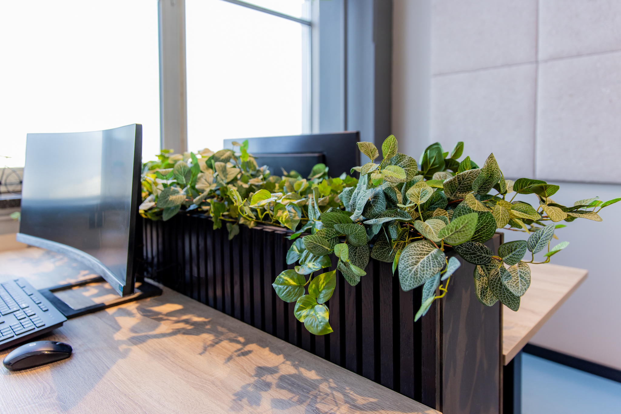 Luxe kunstplanten in een zwarte houten bak op een modern kantoor bureau naast een computermonitor.