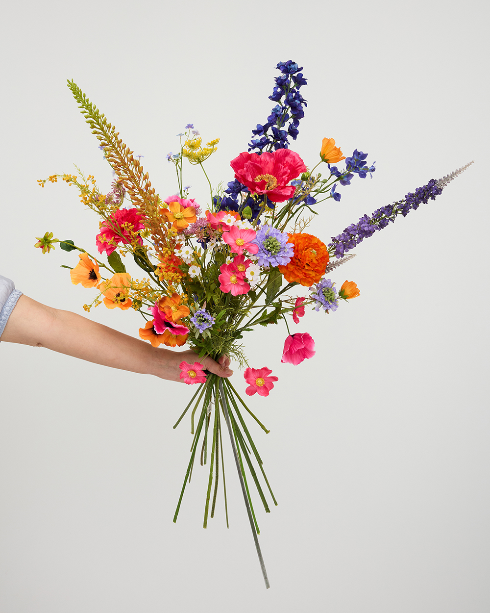 Een hand houdt een kleurrijk boeket van zijden veldbloemen vast tegen een witte achtergrond.