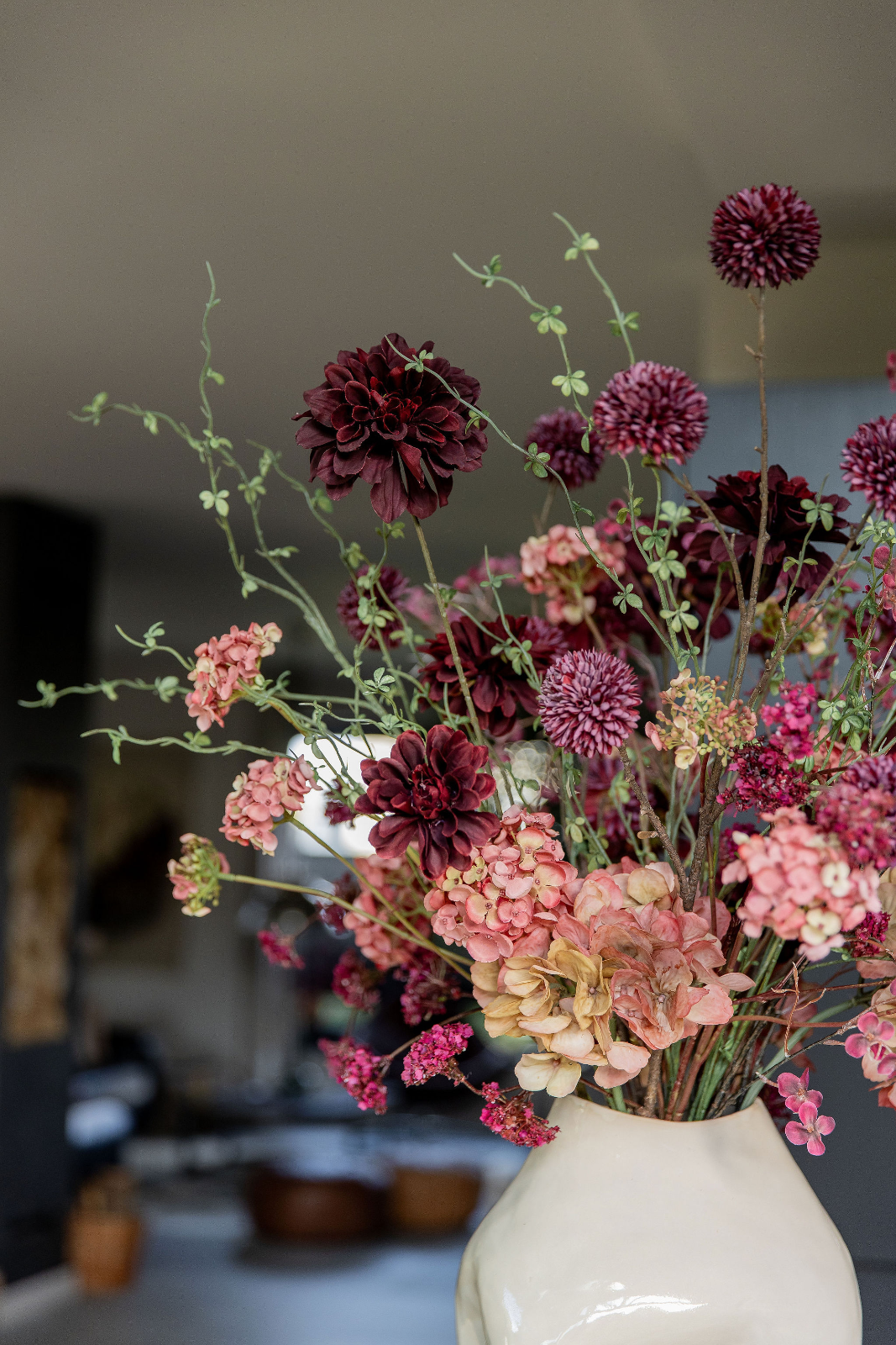Donkerrode dahlia's, paarsrode alliums en zachtroze hortensia's vormen samen een weelderig boeket van zijden bloemen in warme herfsttinten. Kleine roz