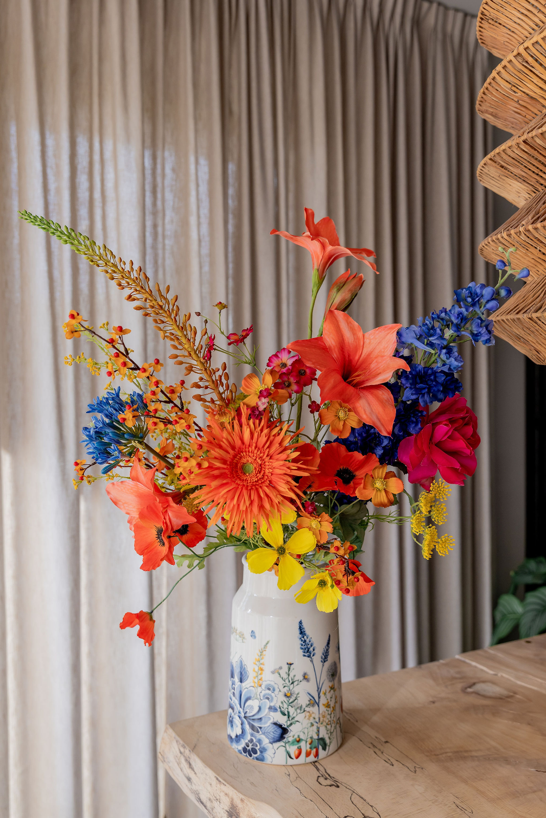 Boeket van zijden bloemen met oranje lelies, een oranje gerbera, rode anemoons, felblauwe delphiniums, agapanthus, een roze roos en gele bloemetjes, i